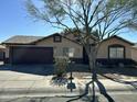 Tan house with a two-car garage, and a mature tree in the front yard at 813 E Long Ave, Buckeye, AZ 85326