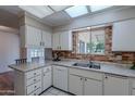 Bright kitchen featuring white cabinets, double sink, and brick accent wall at 10610 W Saratoga Cir, Sun City, AZ 85351