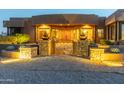 Desert home entrance with stone pillars and ornate gate at dusk at 15405 E Cavedale Dr, Scottsdale, AZ 85262