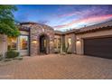 Stone arch entryway, desert landscaping, and three-car garage at sunset at 36701 N Porta Nuova Rd, Scottsdale, AZ 85262
