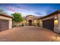 Home exterior with three-car garage, stone archway, and desert landscaping at dusk at 36701 N Porta Nuova Rd, Scottsdale, AZ 85262