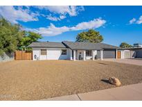 White single story home with gray roof, modern dark garage door, and a gravel front yard at 3334 E Desert Cove Ave, Phoenix, AZ 85028