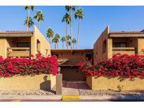 Exterior view of condo building with Spanish-style roof, palm trees, and lush bougainvillea at 8500 E Indian School Rd # 129, Scottsdale, AZ 85251