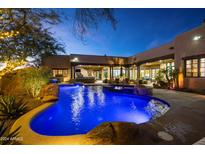 Inviting backyard oasis with a sparkling pool, spa, and outdoor kitchen at dusk at 33296 N Vanishing Trl, Scottsdale, AZ 85266