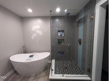 Modern bathroom featuring a soaking tub, glass shower, and gray tile at 5543 Nur Ln, Raleigh, NC 27606