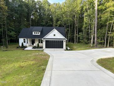 White farmhouse exterior with black garage door and landscaping at 114 Shaman Dr, Louisburg, NC 27549