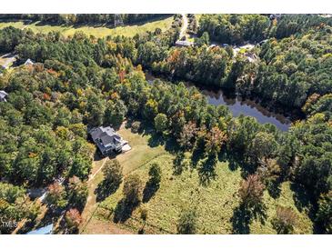 Aerial view of house on a wooded lot with a pond nearby at 488 Colvard Farms Rd, Durham, NC 27713