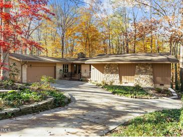 Ranch style home with stone accents and a spacious driveway, nestled in a wooded setting at 1505 Primrose Ln, Cary, NC 27511