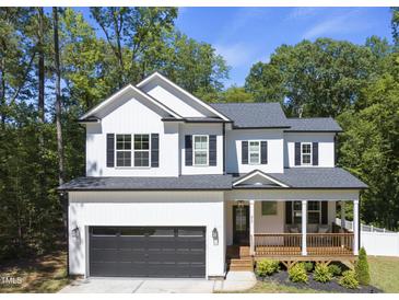 Two-story white farmhouse with black accents, wooden porch, and attached garage at 517 Shawnee Dr, Louisburg, NC 27549