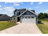 Two-story home with stone and blue siding, white garage door, and landscaped lawn at 83 Oleander Ln, Sanford, NC 27332