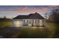 Charming green two-story home at dusk with a two-car garage and large front yard at 7814 Nc 27, Coats, NC 27521