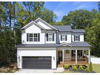 Two-story white farmhouse with black accents, wooden porch, and attached garage at 517 Shawnee Dr, Louisburg, NC 27549