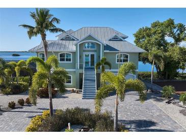 Two-story waterfront home with metal roof, paver driveway, and lush landscaping at 1910 Oregon Trl, Englewood, FL 34224