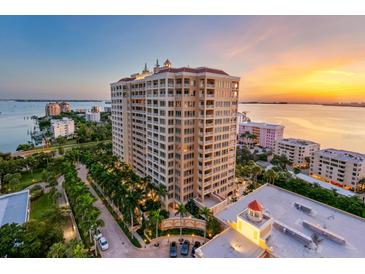 An aerial view showcases a luxury high-rise building, tropical landscaping, and waterfront views at sunset at 35 Watergate Dr # 503, Sarasota, FL 34236