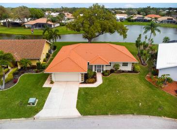 Inviting single-story home featuring a well-manicured lawn, mature landscaping, and a classic tile roof in a lakeside community at 1654 Waxwing Ct, Venice, FL 34293