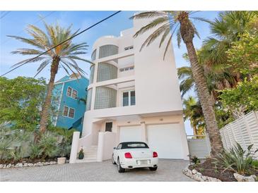 Stunning three-story home showcasing a two-car garage, glass-block windows, and lush landscaping with palm trees at 648 Beach Rd, Sarasota, FL 34242