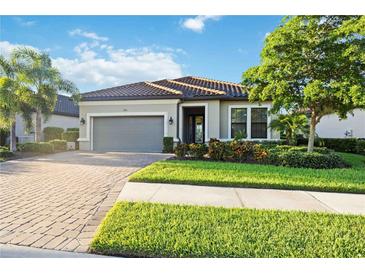 Single-story home with gray garage door, lush landscaping, and brick paver driveway at 5585 Semolino St, Nokomis, FL 34275