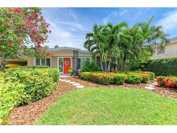 Charming home with lush landscaping, including palm trees, colorful flowers, and a vibrant orange front door at 136 Crescent Dr, Anna Maria, FL 34216