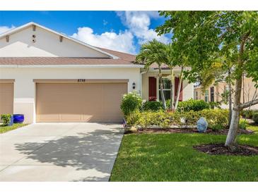 Tan house with two-car garage, landscaping, and Buddha statue at 8798 Tuscany Isles Dr, Punta Gorda, FL 33950