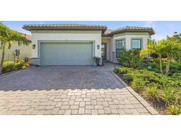 Inviting home featuring a two-car garage, beautiful landscaping, and a brick-paved driveway at 14480 Eagle Branch Dr, Nokomis, FL 34275