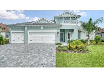 Two-story home with light teal exterior, three car garage, and landscaping at 12420 Destin Loop, Venice, FL 34293