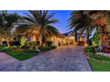 Stunning exterior showcasing lush landscaping, large palms, and a paver driveway leading to a well-lit home at 7928 Matera Ct, Lakewood Ranch, FL 34202