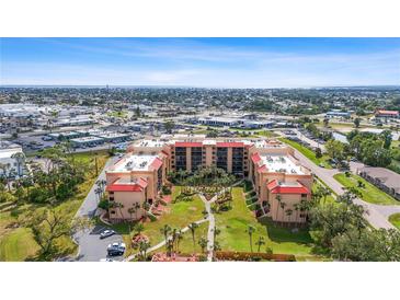 Stunning aerial view of condo building with red roof, lush landscaping, and ocean view in distance at 3006 Caring Way # 224, Port Charlotte, FL 33952