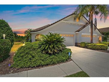Beautiful home featuring a well-manicured lawn, tropical foliage, and a two-car garage at 7011 Woodmore Ter, Lakewood Ranch, FL 34202