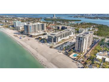 Expansive aerial view of beachfront condos with lush landscaping, a sparkling pool, and pristine sandy beach at 1102 Benjamin Franklin Dr # 409, Sarasota, FL 34236