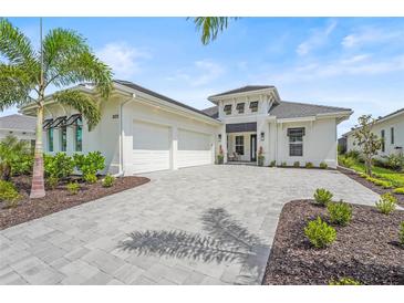 Beautiful home featuring a three-car garage, light exterior, and paver driveway surrounded by lush landscaping at 8332 Sea Glass Ct, Sarasota, FL 34240