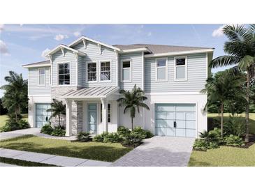 Inviting two-story coastal home showcasing a two-car garage, light blue wood siding, stone accents, and lush landscaping at 5019 Commonwealth Dr, Sarasota, FL 34242