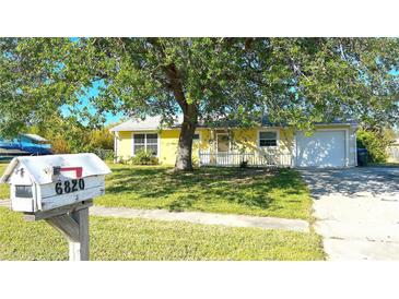 House exterior featuring a yellow house, driveway, and mature tree at 6820 Myrtlewood Rd, North Port, FL 34287