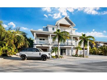 Elegant two-story home boasts balconies, palm trees, and a pristine white exterior, creating a luxurious tropical ambiance at 598 Lyons Ln, Longboat Key, FL 34228