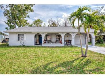 Ranch-style home with covered porch, mature landscaping, and a two-car garage at 13479 Newport Ave, Port Charlotte, FL 33981