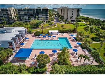 Aerial view of a large pool surrounded by lounge chairs, umbrellas, palm trees, and manicured landscaping at 1085 Gulf Of Mexico Dr # 301, Longboat Key, FL 34228