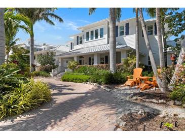 Charming two-story home with tropical landscaping, brick driveway, and inviting orange Adirondack chairs at 116 50Th St, Holmes Beach, FL 34217