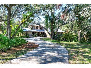 House with circular driveway, surrounded by lush landscaping and mature trees at 4938 Hubner Cir, Sarasota, FL 34241