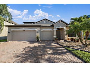 Beige two-story house with two-car garage, landscaping, and brick driveway at 13325 Sunset Shore Cir, Riverview, FL 33579