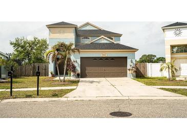 Two story blue home featuring a large garage, well manicured lawn, and palm trees at 731 Cristelle Jean Dr, Ruskin, FL 33570