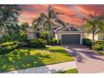 Beautiful home featuring a well-manicured lawn, palm trees, and a brick driveway under a captivating sky at 942 Preservation St, Bradenton, FL 34208