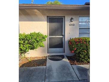 Exterior view of a light beige building with a dark door, address 1313, and landscaping at 1313 54Th E Ave # 1313, Bradenton, FL 34203