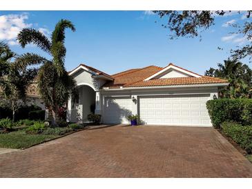 Charming single-story home featuring a brick driveway, white garage doors, tropical landscaping, and a red tile roof at 9203 Winter Harbour Way, Bradenton, FL 34212