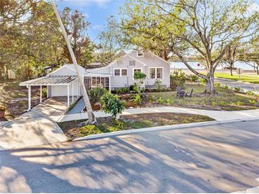 Charming gray home features covered parking, screened porch and mature landscaping on a sunny day at 514 Riverside E Dr, Bradenton, FL 34208