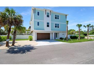 Beautiful three-story coastal home with a light blue facade, complemented by a two-car garage, and lush palm trees at 630 Companion Way, Longboat Key, FL 34228