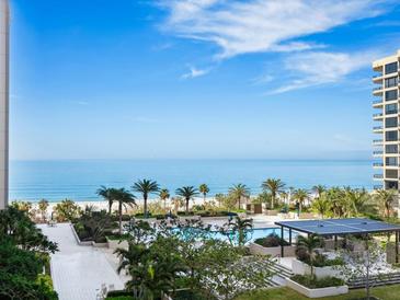 Stunning oceanfront view featuring a swimming pool, lush landscaping and palm trees in an idyllic beach setting at 1211 Gulf Of Mexico Dr # 301, Longboat Key, FL 34228