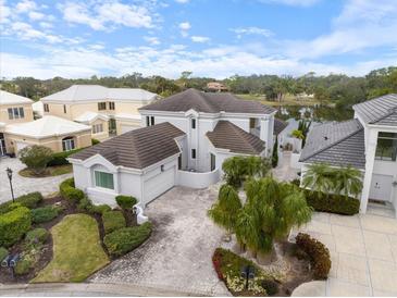 Stunning aerial view of a luxurious two-story home with a tile roof, paver driveway, and lush landscaping, with lake view at 7716 Club Ln, Sarasota, FL 34238