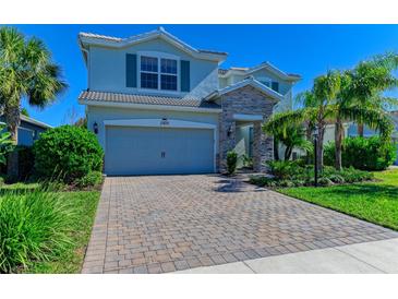 Two-story home boasts a stone-accented entrance, a two-car garage, and a brick paved driveway, complemented by lush landscaping at 3409 Anchor Bay Trl, Lakewood Ranch, FL 34211