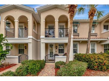 Charming townhome exterior with arched entryway, balcony, tidy landscaping, and brick walkway at 5972 Giardino Ln, Sarasota, FL 34232