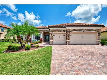 Well-manicured home exterior with a brick driveway, lush green lawn, and charming landscaping at 20686 Valprato Ct, Venice, FL 34293
