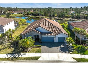 Beautiful aerial view of home with tile roof, three-car garage, and a well-manicured lawn in a quiet neighborhood with a pond view at 6625 Dovekey Dr, Sarasota, FL 34241